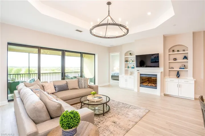 Living room featuring a tray ceiling, a chandelier, light wood-style flooring, built in features, and recessed lighting