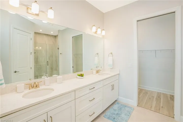Full bathroom with double vanity, a stall shower, a spacious closet, and tile patterned flooring