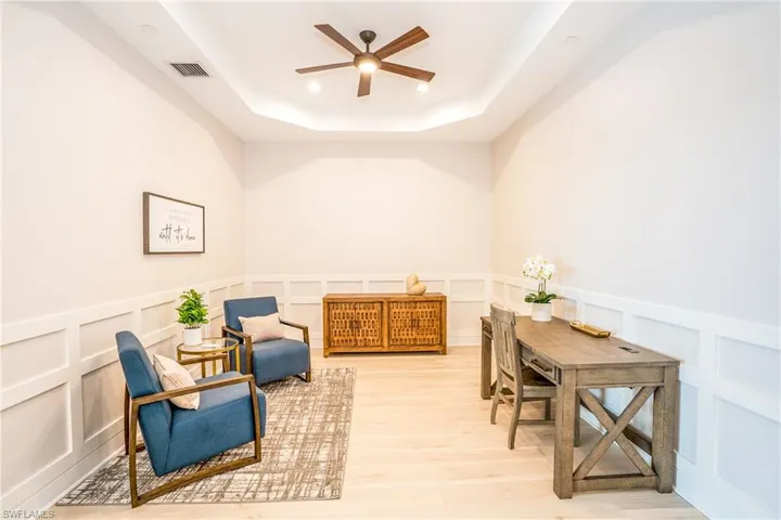 Living area with a ceiling fan, a decorative wall, a raised ceiling, light wood finished floors, and wainscoting