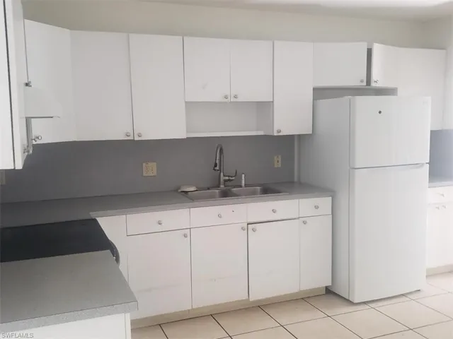 Kitchen featuring white cabinets, freestanding refrigerator, tasteful backsplash, light countertops, and range