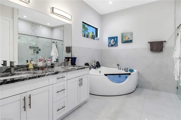 Full bathroom featuring double vanity, a tub with jets, a shower stall, tile walls, and wainscoting