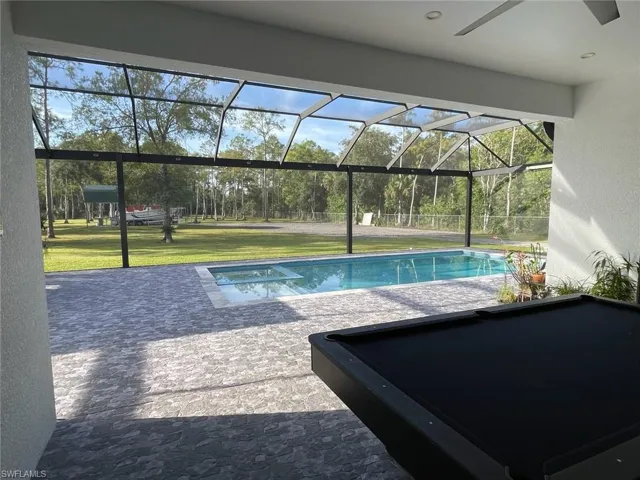 Outdoor pool with screen enclosure, a patio area, and a lawn