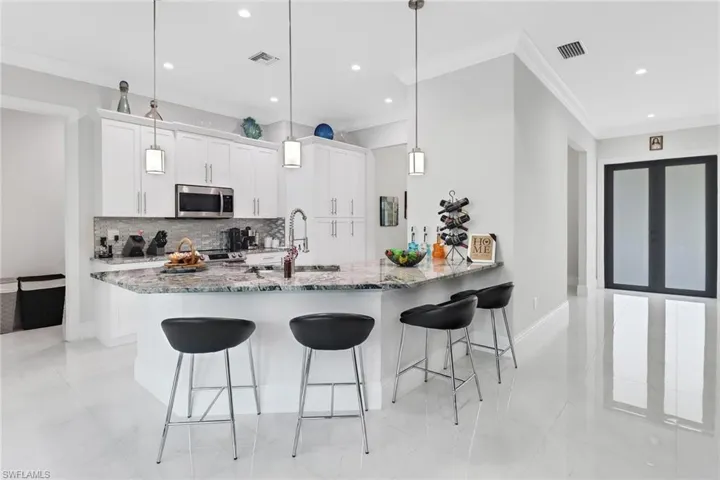 Kitchen with a peninsula, a breakfast bar, decorative backsplash, white cabinets, and stainless steel microwave