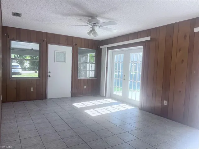 Spare room featuring light tile floors, a textured ceiling, ceiling fan, and wood walls