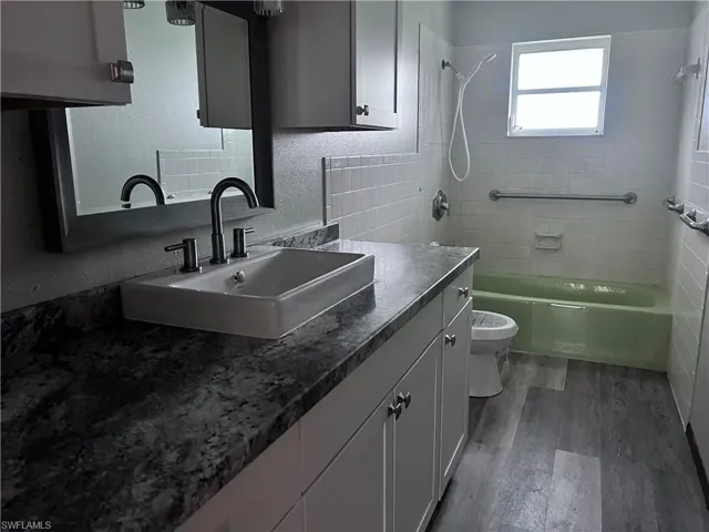 Full bathroom with vanity, toilet, tiled shower / bath combo, and hardwood / wood-style flooring
