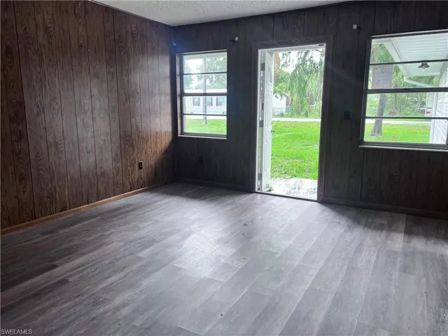 Empty room with wood walls, dark hardwood / wood-style flooring, and a textured ceiling