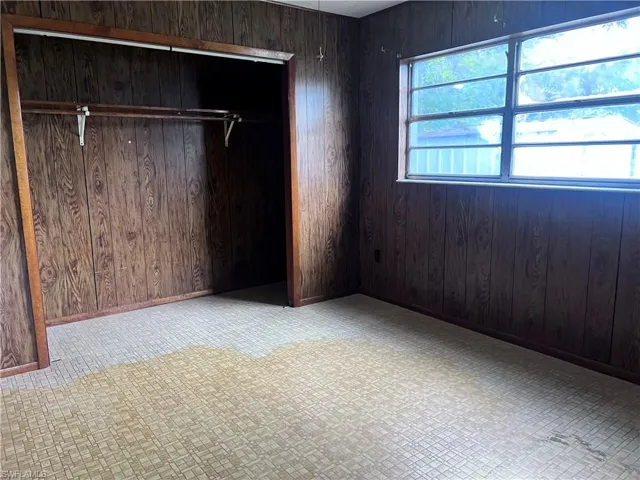 Unfurnished bedroom with light tile flooring, a closet, and wooden walls