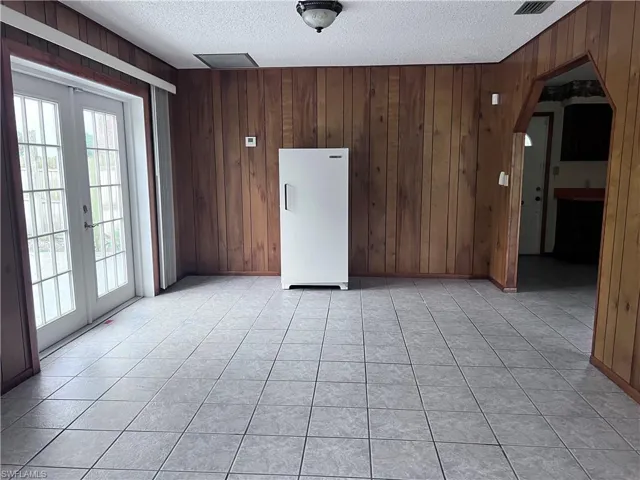 Spare room with a wealth of natural light, wood walls, light tile flooring, and a textured ceiling