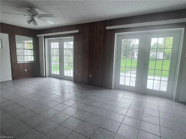 Empty room with ceiling fan, tile flooring, french doors, and wood walls