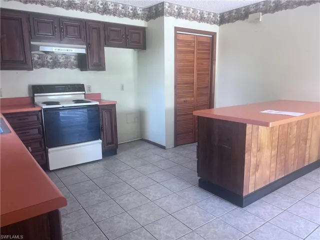 Kitchen featuring dark brown cabinetry, electric range, and light tile flooring