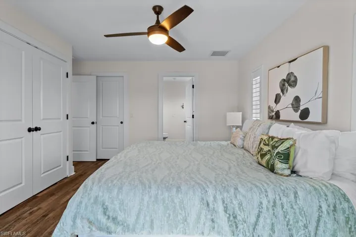 Bedroom with ensuite bathroom, dark wood-type flooring, and ceiling fan