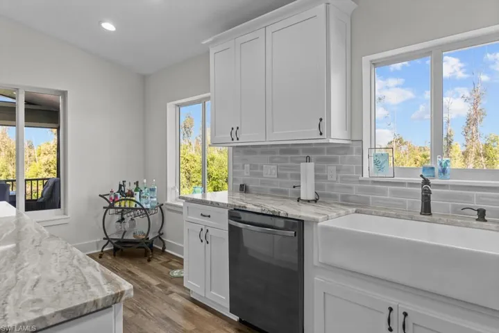 Kitchen with white cabinetry, sink, backsplash, stainless steel dishwasher, and light stone counters