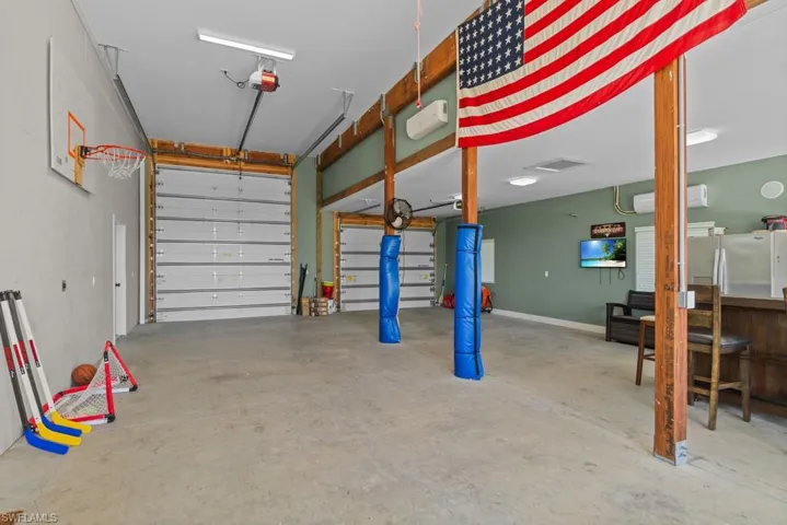 Garage with stainless steel refrigerator, a garage door opener, and an AC wall unit