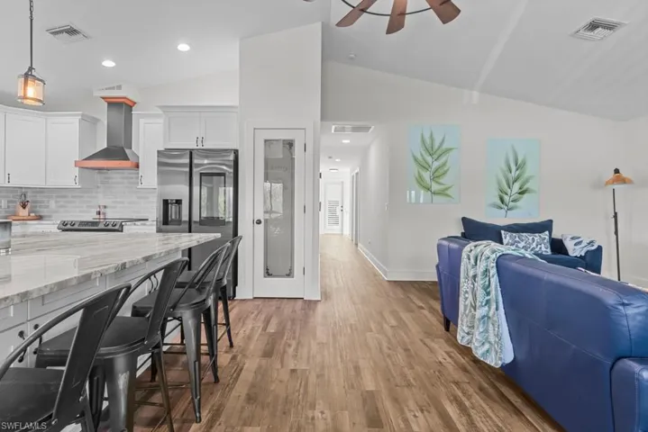 Kitchen featuring lofted ceiling, wall chimney exhaust hood, hanging light fixtures, white cabinets, and backsplash
