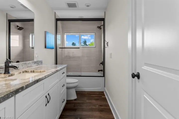 Full bathroom with toilet, vanity, combined bath / shower with glass door, and hardwood / wood-style floors