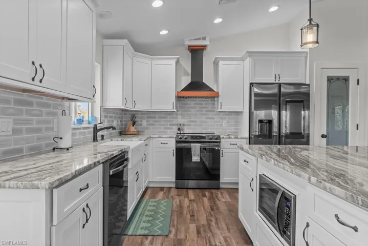 Kitchen featuring white cabinets, vaulted ceiling, stainless steel appliances, and wall chimney exhaust hood