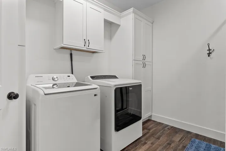 Clothes washing area with washer and dryer, dark hardwood / wood-style flooring, and cabinets
