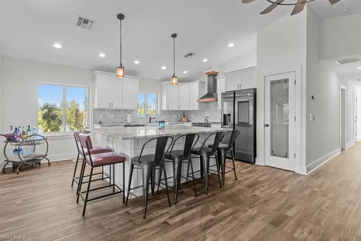 Kitchen featuring white cabinets, lofted ceiling, wall chimney exhaust hood, and stainless steel fridge with ice dispenser