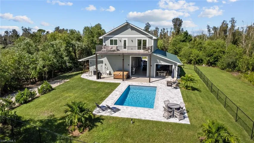 Back of house featuring a balcony, a swimming pool with hot tub, a patio area, and a lawn