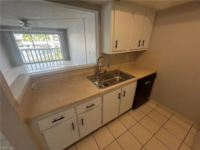 Kitchen featuring white cabinetry, light countertops, light tile patterned floors, and black dishwasher