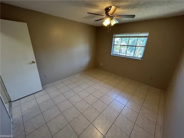 Unfurnished room featuring a textured ceiling, light tile patterned flooring, and a ceiling fan
