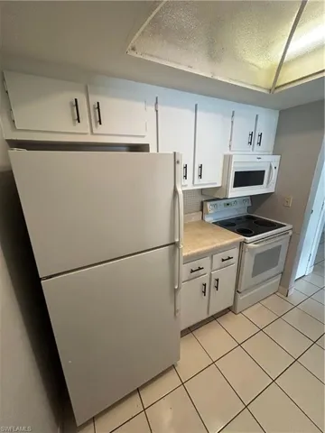 Kitchen featuring white appliances, white cabinetry, light tile patterned flooring, light countertops, and a textured ceiling