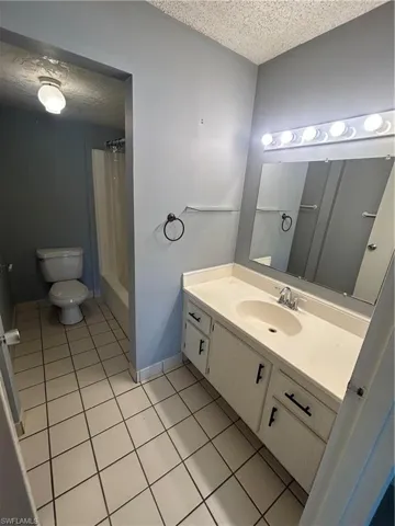 Bathroom with a textured ceiling, vanity, light tile patterned floors, and shower / bathtub combination with curtain