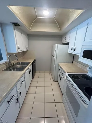 Kitchen featuring range, a tray ceiling, white cabinets, light countertops, and light tile patterned flooring