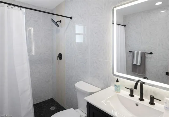 Contemporary bathroom featuring a black vanity with a white countertop and undermount sink, matte black faucet, and an illuminated mirror
