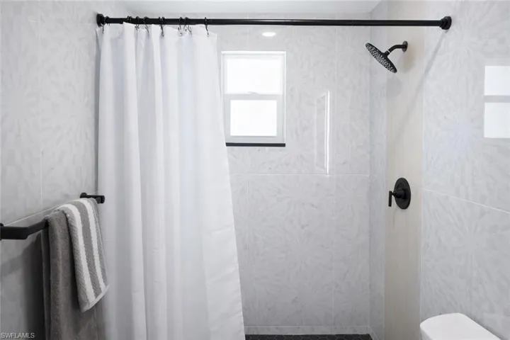 Shower area featuring contemporary patterned wall tiling, a matte black rainfall showerhead, and coordinating matte black fixtures