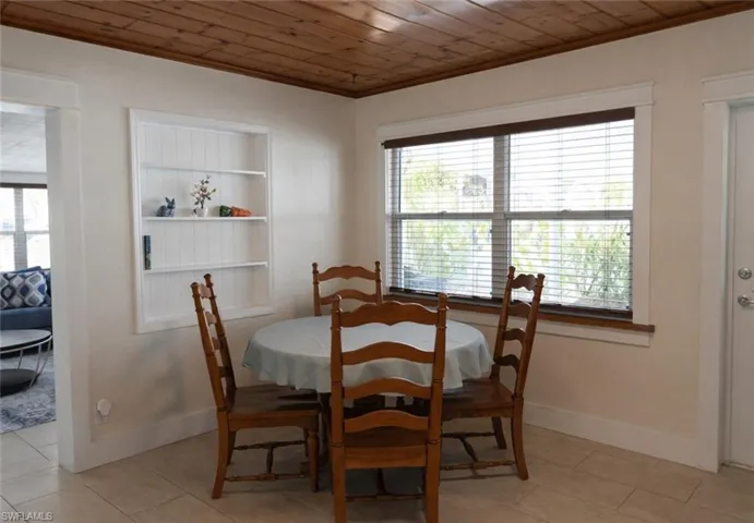 Dining area featuring a wood-panel ceiling, built-in shelving, a double window with wood-finish blinds, and tile flooring