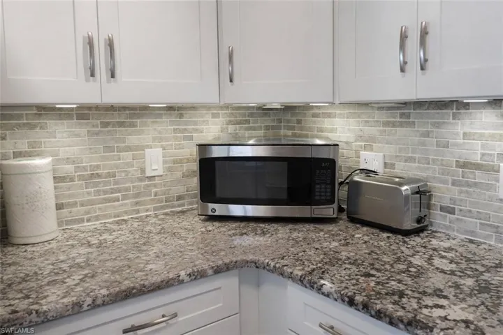 Kitchen featuring granite-style countertops, white shaker-style cabinetry with brushed nickel hardware, and a mosaic tile backsplash