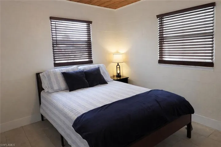 Bedroom featuring two windows with wood-finish blinds, light-toned walls, and a wood-panel ceiling