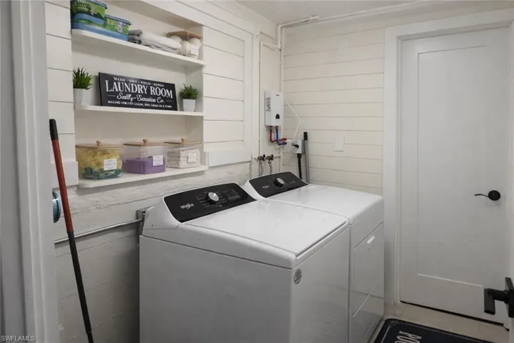 Dedicated laundry area featuring a white shaker-style door, shiplap wall paneling, built-in shelving, and a water heater