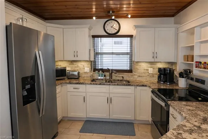 Kitchen featuring a wood-finish ceiling, stainless steel appliances, white cabinetry, a tiled backsplash, and granite countertops