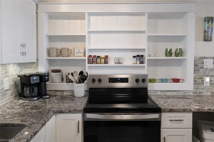 Modern kitchen featuring white cabinetry, granite-finish countertops, stainless steel range, and a tiled backsplash