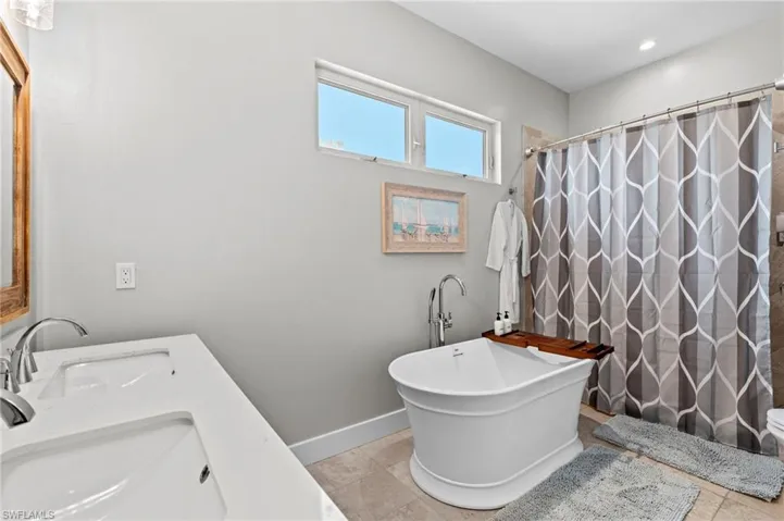 Bathroom with a shower with curtain, tile patterned floors, and a freestanding bath