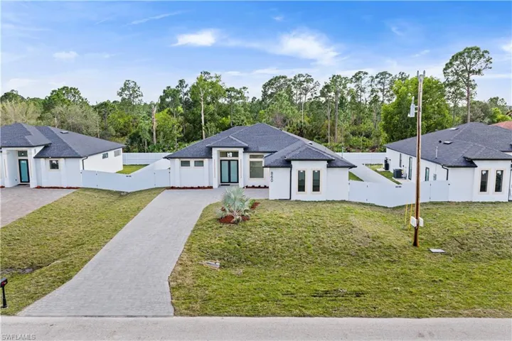 View of front of home featuring decorative driveway, stucco siding, a gate, and view of wooded area