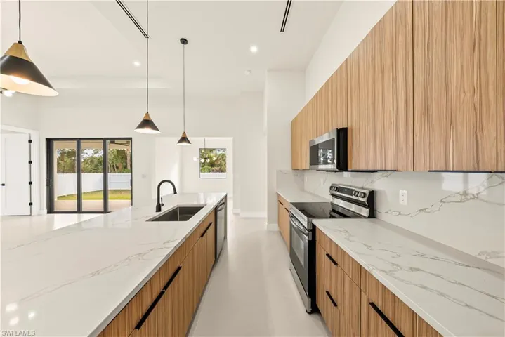 Kitchen featuring modern cabinets, light stone counters, stainless steel appliances, pendant lighting, and tasteful backsplash