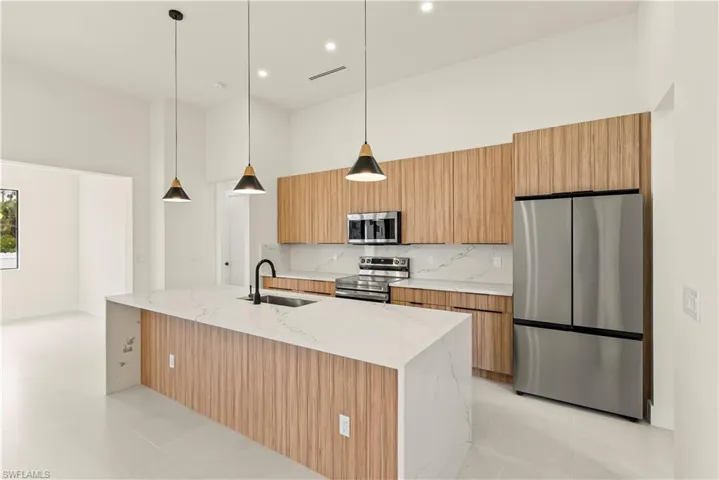 Kitchen with stainless steel appliances, light stone countertops, a high ceiling, hanging light fixtures, and an island with sink