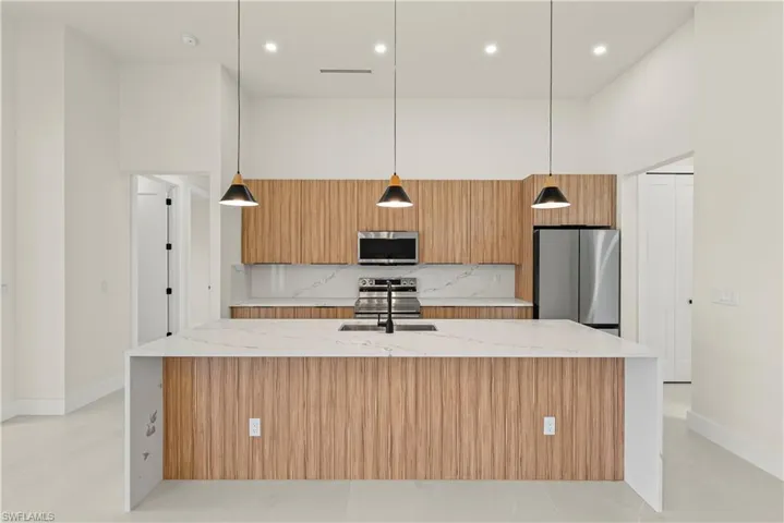 Kitchen featuring light stone countertops, hanging light fixtures, a spacious island, stainless steel appliances, and a high ceiling