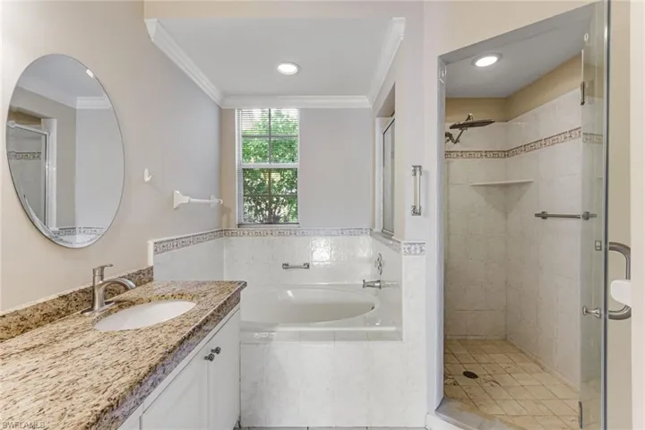 Bathroom featuring a built-in tub, separate glass-enclosed shower, vanity with granite countertop, integrated sink, and an oval mirror