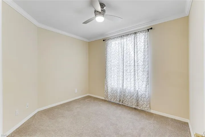 Carpeted room featuring a ceiling fan with integrated lighting, crown molding, and a window with sheer curtains