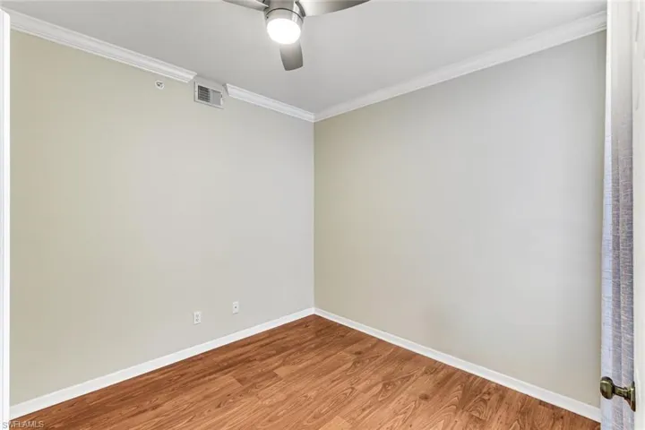 Room with wood-finish flooring, light neutral wall paint, and white crown molding