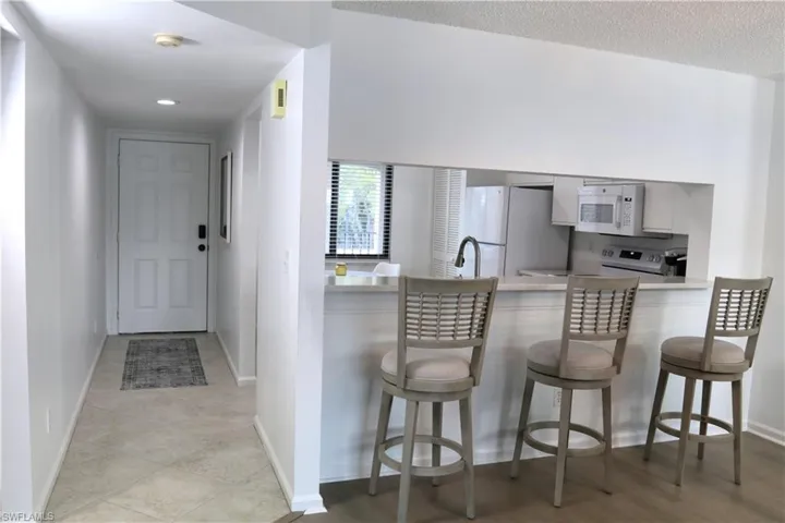 Kitchen featuring white appliances, a peninsula, white cabinets, a breakfast bar area, and recessed lighting