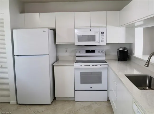 Kitchen with white appliances, white cabinets, and light stone countertops
