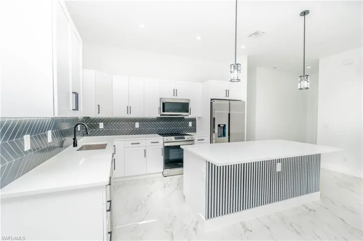 Kitchen featuring white cabinets, stainless steel appliances, decorative light fixtures, light marble finish floors, and recessed lighting