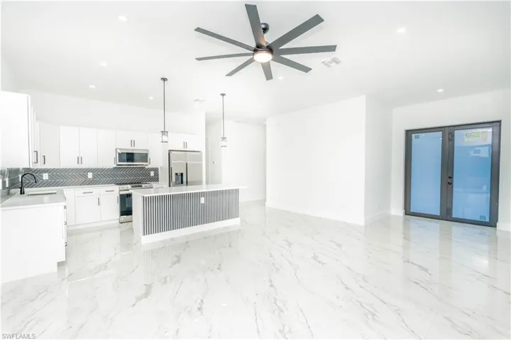 Kitchen featuring white cabinets, hanging light fixtures, stainless steel appliances, open floor plan, and light marble finish floors