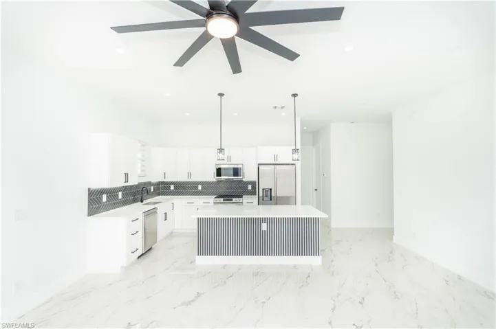 Kitchen with white cabinets, appliances with stainless steel finishes, hanging light fixtures, a kitchen island, and tasteful backsplash