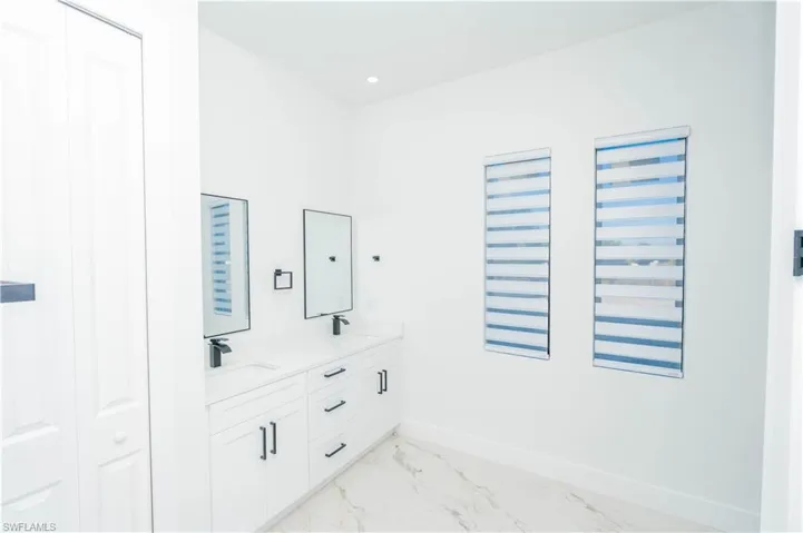 Full bath with double vanity, a closet, light marble finish flooring, and recessed lighting